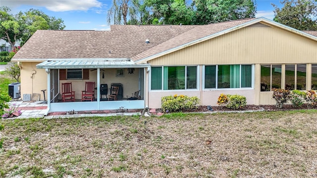 rear view of house with a shingled roof, stucco siding, central AC unit, a yard, and a sunroom