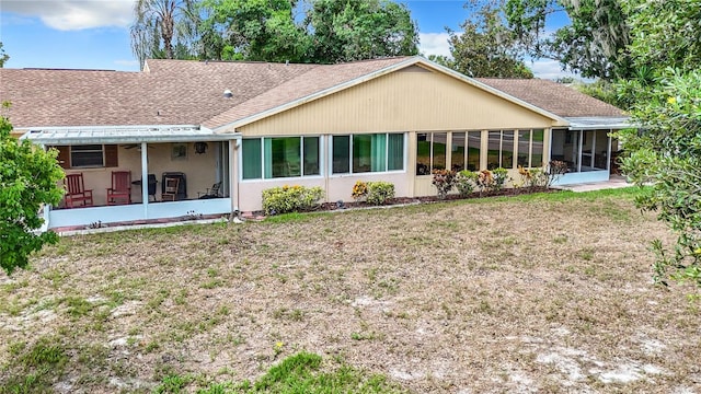 rear view of property with a yard, roof with shingles, and a sunroom