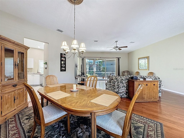 dining room with baseboards, visible vents, light wood-style flooring, a textured ceiling, and ceiling fan with notable chandelier