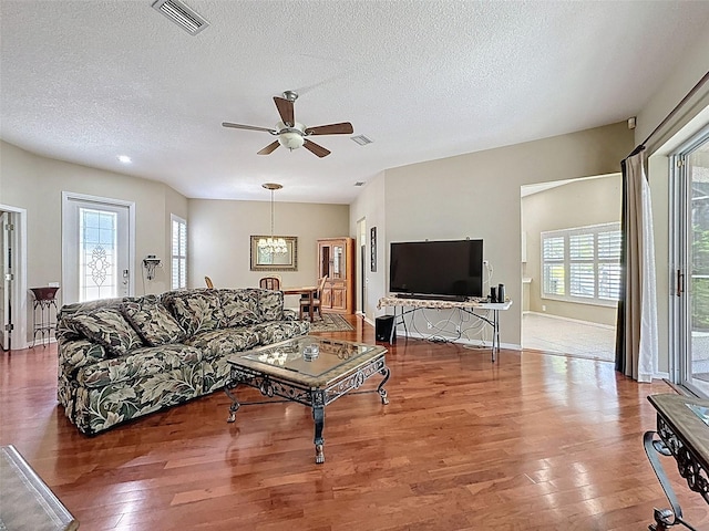 living room featuring visible vents, ceiling fan with notable chandelier, a textured ceiling, wood-type flooring, and baseboards