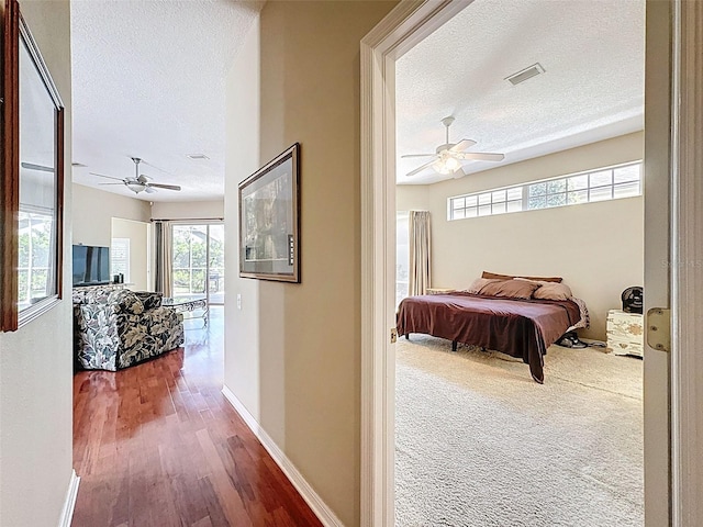 hall featuring wood finished floors, baseboards, visible vents, and a textured ceiling