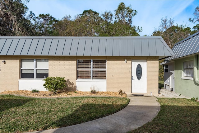 view of front of house featuring metal roof, brick siding, a front lawn, and a standing seam roof