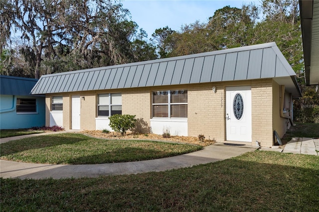 view of front of house featuring a standing seam roof, a front yard, brick siding, and metal roof