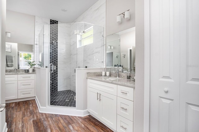 full bath featuring a sink, wood finished floors, two vanities, and a stall shower