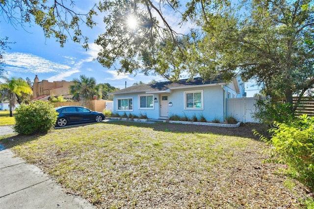 view of front of property with stucco siding, a front lawn, and fence