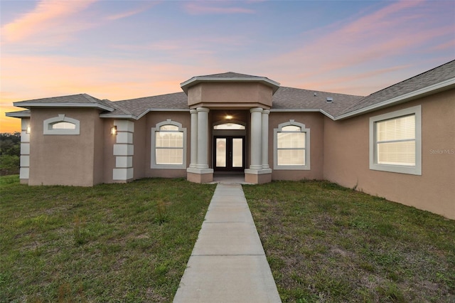 view of front of property featuring a yard, french doors, roof with shingles, and stucco siding