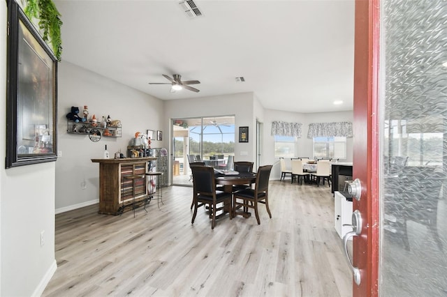 dining room with baseboards, visible vents, light wood-style flooring, ceiling fan, and a bar