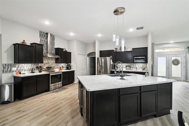 kitchen featuring visible vents, arched walkways, a sink, appliances with stainless steel finishes, and wall chimney range hood