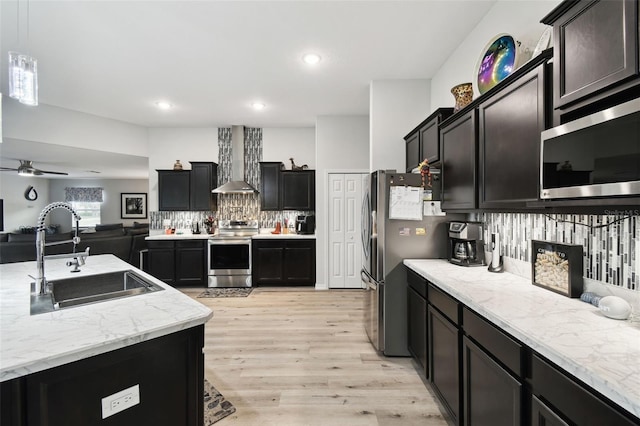 kitchen featuring backsplash, open floor plan, stainless steel appliances, wall chimney exhaust hood, and a sink