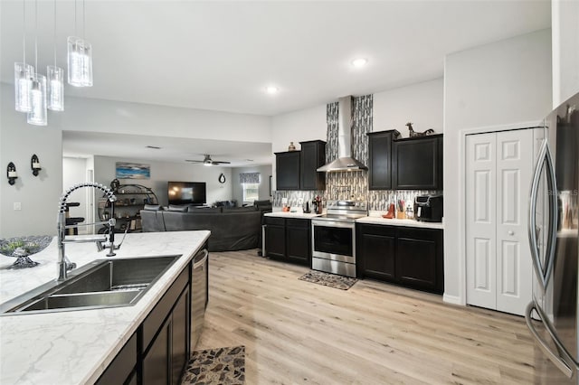 kitchen featuring a sink, stainless steel appliances, open floor plan, wall chimney exhaust hood, and dark cabinets