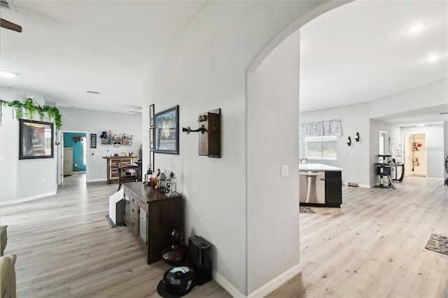 hall featuring arched walkways, light wood finished floors, and baseboards