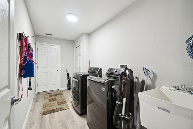 laundry area with visible vents, light wood-style flooring, a sink, separate washer and dryer, and laundry area