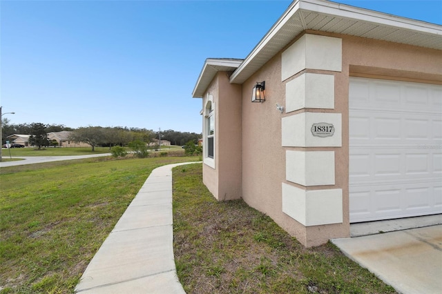 view of side of property featuring stucco siding, a yard, and an attached garage