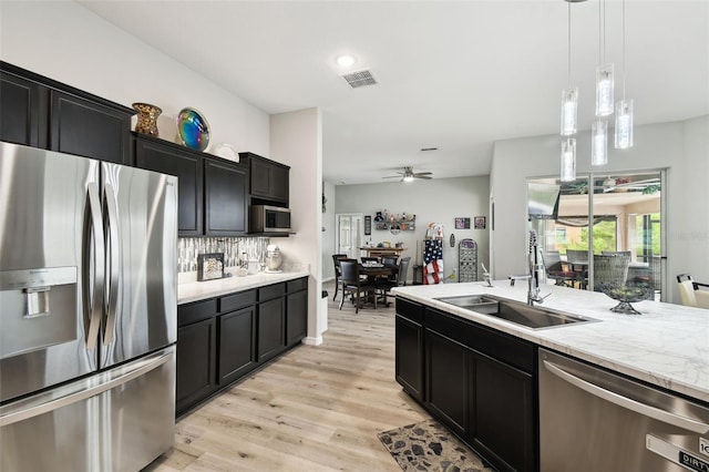 18317 Treehaven Dr, Hudson, FL 34667 - kitchen featuring stainless steel appliances, a sink, light wood-style floors, dark cabinetry, and a ceiling fan