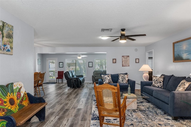 living room featuring ceiling fan, visible vents, a textured ceiling, and wood finished floors