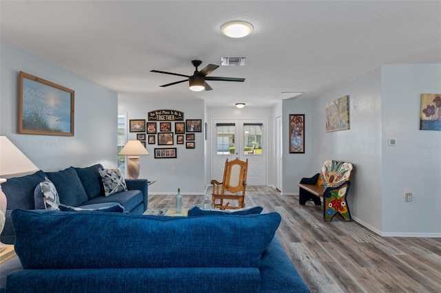 living area featuring a ceiling fan, wood finished floors, visible vents, baseboards, and french doors