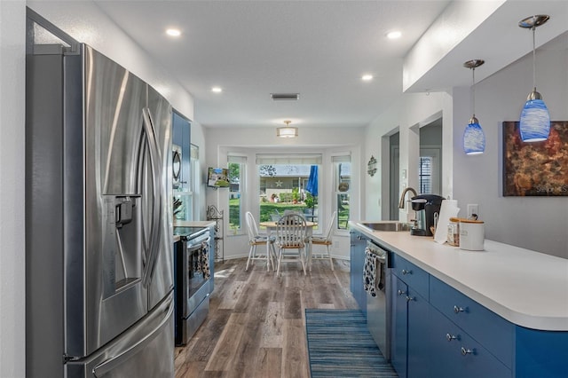 kitchen with blue cabinetry, appliances with stainless steel finishes, dark wood-style floors, and a sink