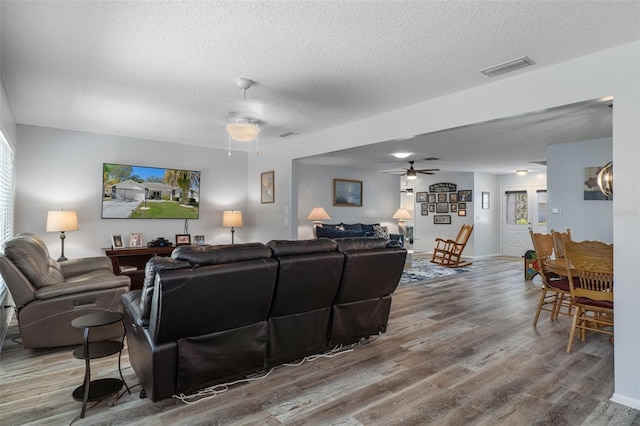 living room featuring ceiling fan, visible vents, a textured ceiling, and wood finished floors