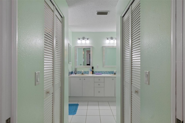 bathroom with double vanity, a closet, a textured ceiling, and tile patterned flooring