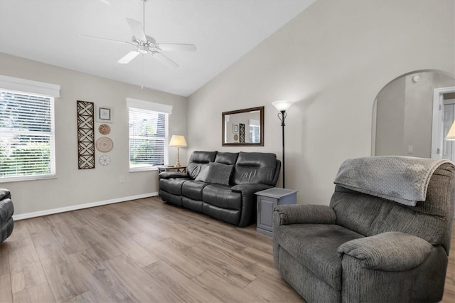 living room featuring baseboards, light wood finished floors, arched walkways, ceiling fan, and vaulted ceiling