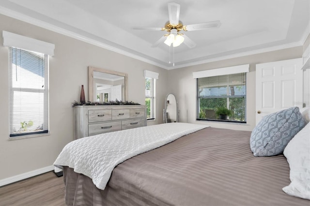 bedroom featuring a tray ceiling, baseboards, wood finished floors, and ornamental molding