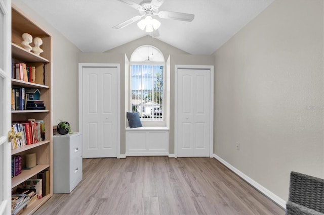 interior space featuring baseboards, multiple closets, vaulted ceiling, wood finished floors, and a ceiling fan