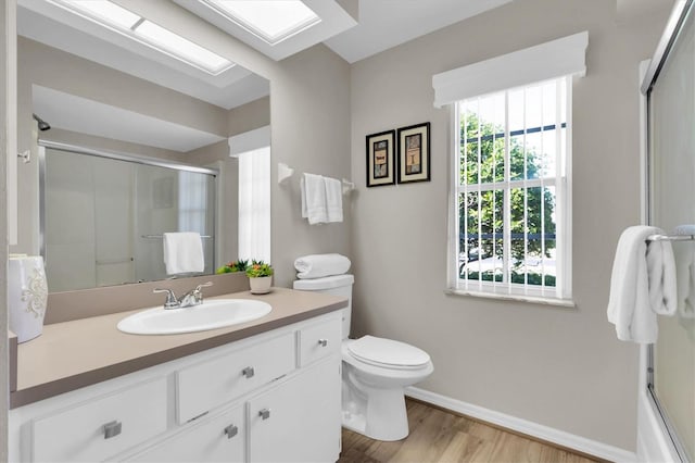 bathroom featuring toilet, a shower with door, wood finished floors, a skylight, and vanity