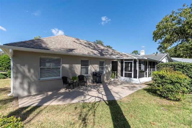 back of house featuring roof with shingles, a sunroom, stucco siding, a patio area, and a lawn