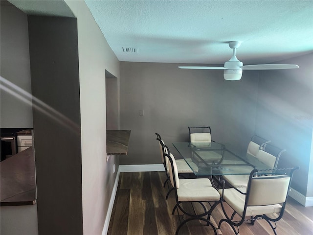 dining space with baseboards, a textured ceiling, visible vents, ceiling fan, and wood finished floors