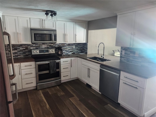 kitchen featuring stainless steel appliances, a sink, dark countertops, dark wood-style floors, and white cabinets