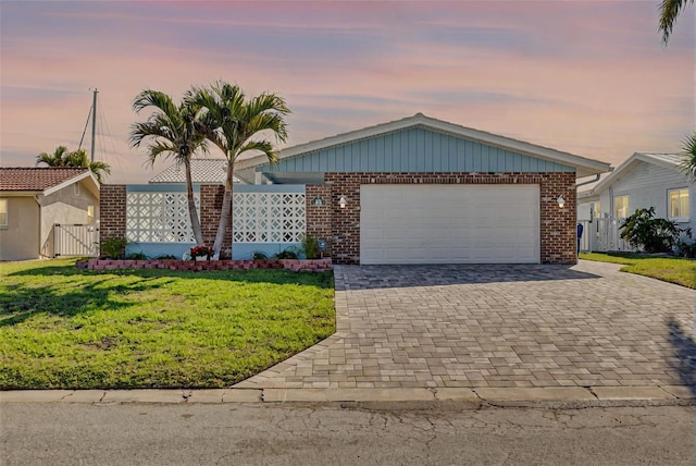 view of front of house featuring brick siding, a front lawn, decorative driveway, an attached garage, and a gate