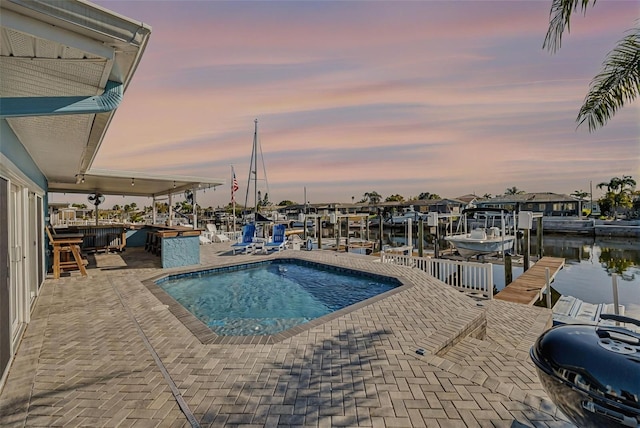 pool at dusk featuring a patio area, boat lift, a boat dock, and a water view