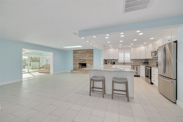 kitchen featuring visible vents, open floor plan, stainless steel appliances, white cabinets, and decorative backsplash