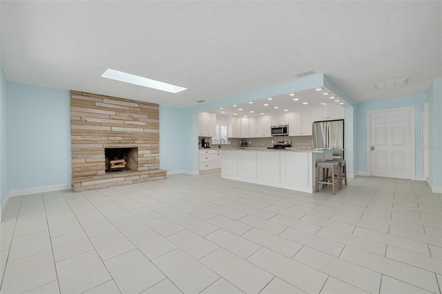 unfurnished living room featuring visible vents, a fireplace, a skylight, and baseboards