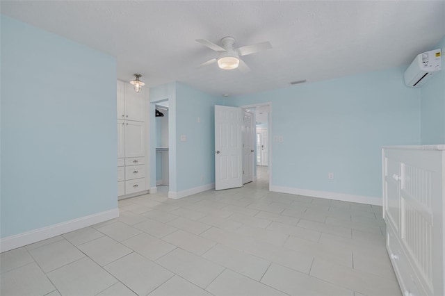 unfurnished bedroom with a walk in closet, visible vents, a wall mounted AC, baseboards, and ceiling fan