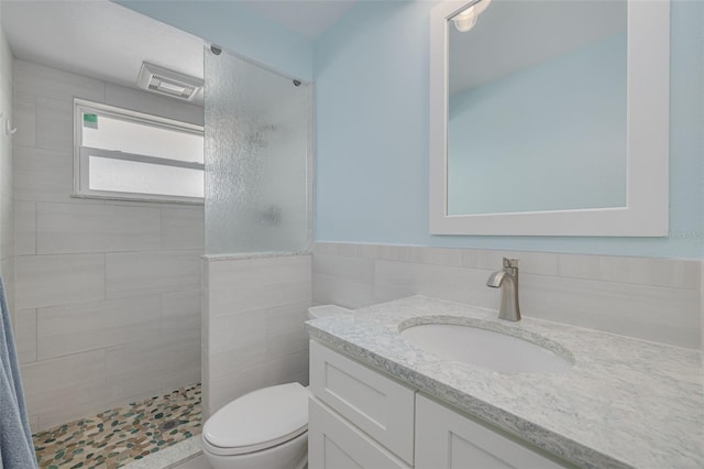 bathroom with visible vents, toilet, tile walls, tiled shower, and vanity