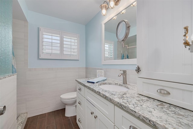 bathroom featuring vanity, wood tiled floor, a tile shower, tile walls, and toilet