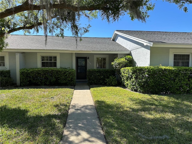 ranch-style house featuring a front lawn, roof with shingles, and stucco siding