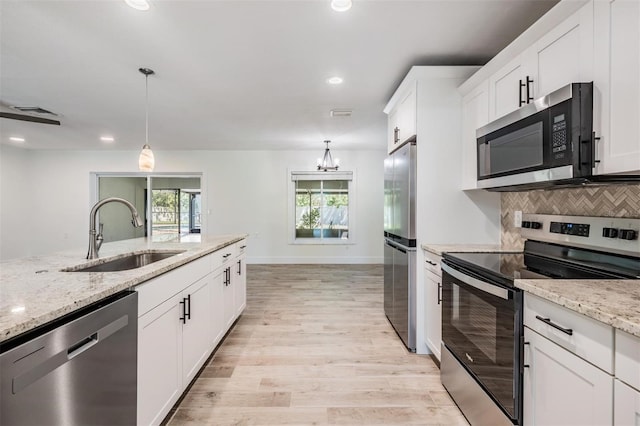 kitchen with light stone counters, a sink, decorative backsplash, stainless steel appliances, and white cabinets