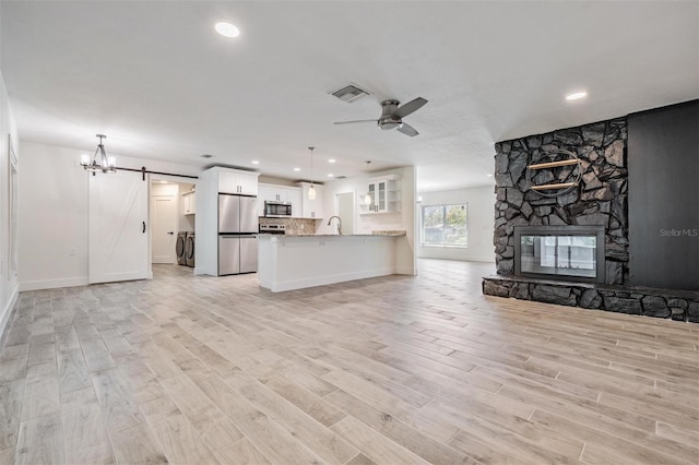 unfurnished living room with light wood finished floors, ceiling fan with notable chandelier, a sink, a barn door, and washing machine and dryer