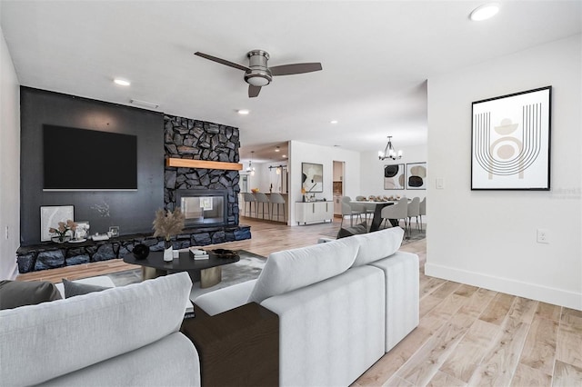 living area with a fireplace, light wood-style flooring, ceiling fan with notable chandelier, and baseboards