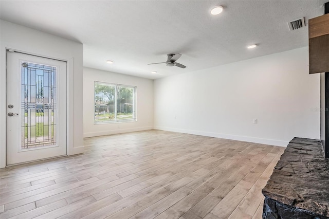 unfurnished living room with light wood finished floors, visible vents, baseboards, a textured ceiling, and a ceiling fan