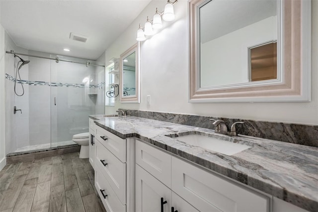 bathroom with wood finished floors, a stall shower, toilet, and a sink