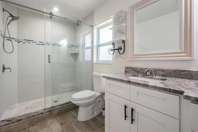 bathroom with a shower stall, toilet, vanity, and wood finished floors