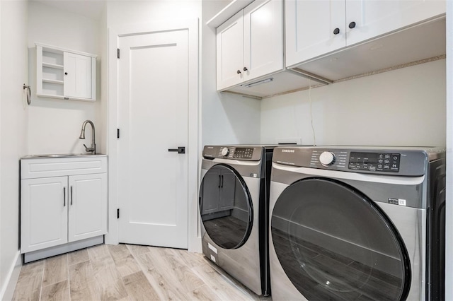 clothes washing area featuring washer and clothes dryer, cabinet space, light wood-style floors, and a sink