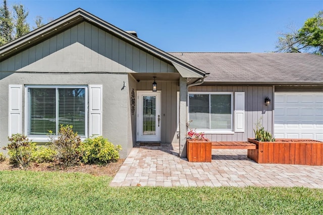 doorway to property with an attached garage and a shingled roof