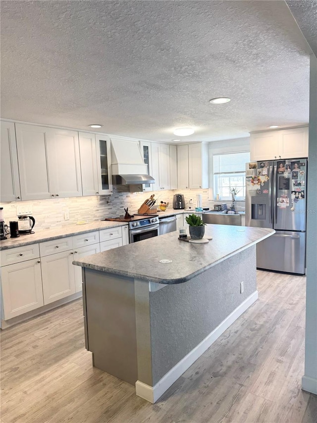 kitchen with a kitchen island, light wood-style floors, appliances with stainless steel finishes, wall chimney exhaust hood, and white cabinets