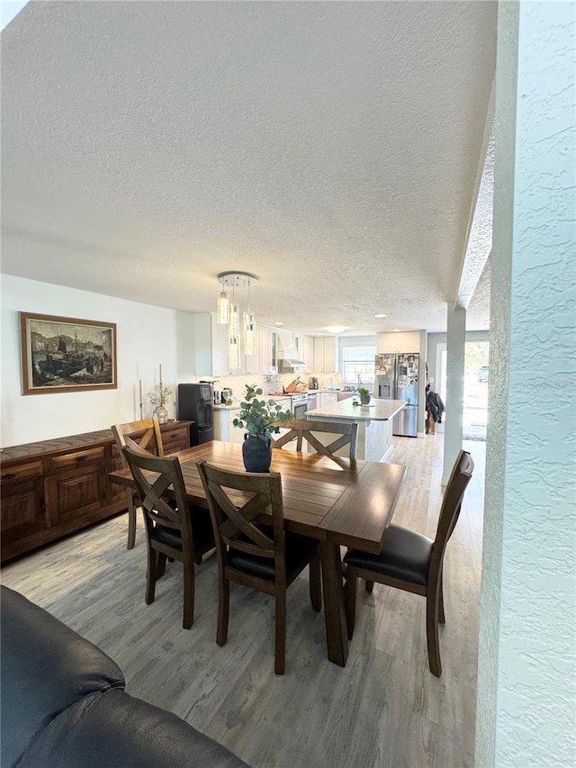 dining room featuring light wood-type flooring, a textured ceiling, and a textured wall