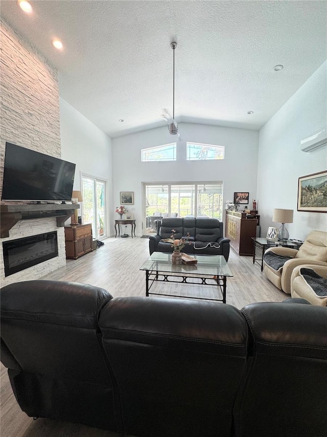 living area with high vaulted ceiling, light wood-type flooring, a textured ceiling, and a fireplace