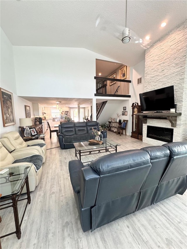 living room with wood finished floors, visible vents, high vaulted ceiling, stairs, and a stone fireplace